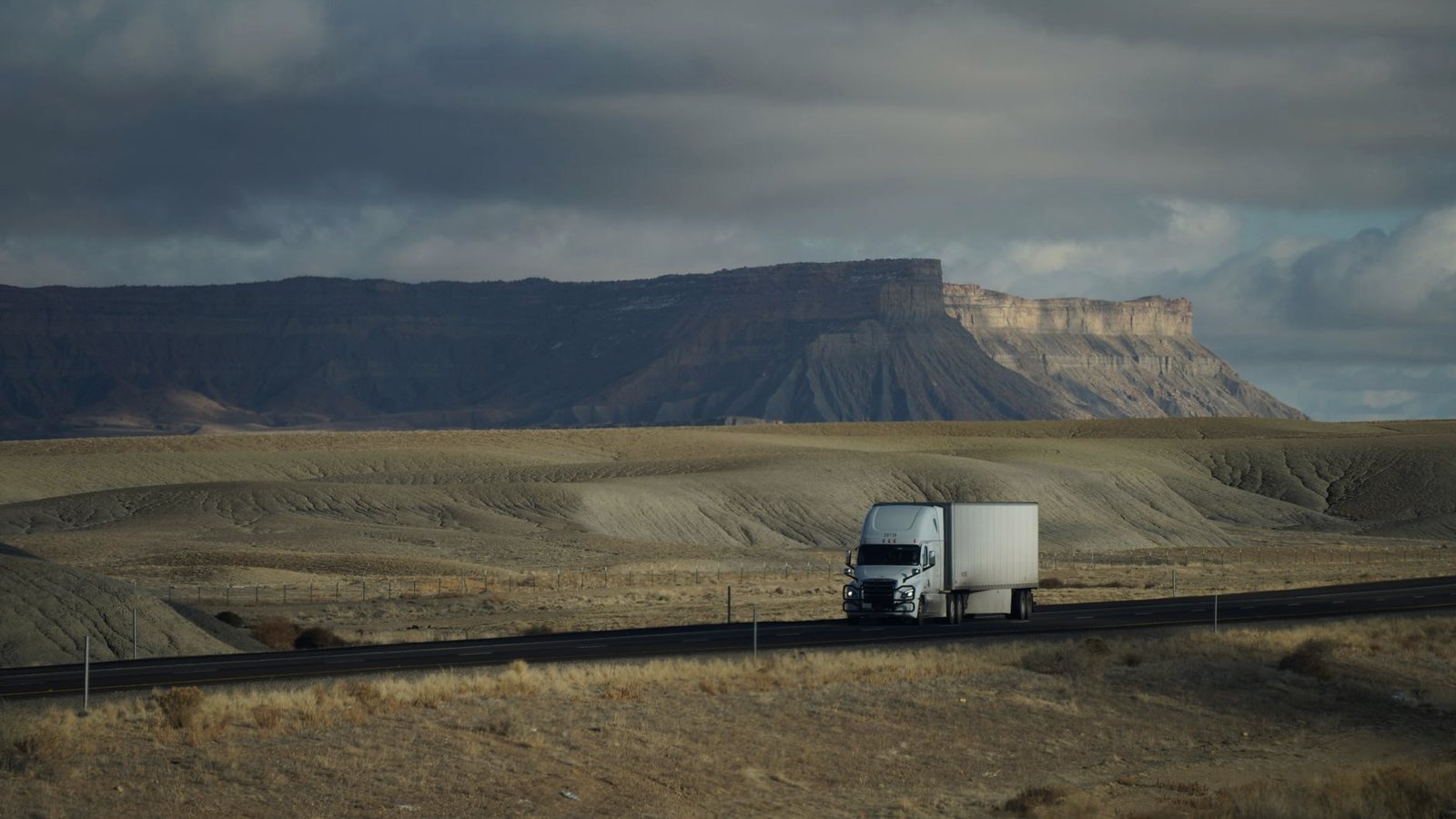 Single tractor-trailer on a highway crossing a desert under a cloudy sky