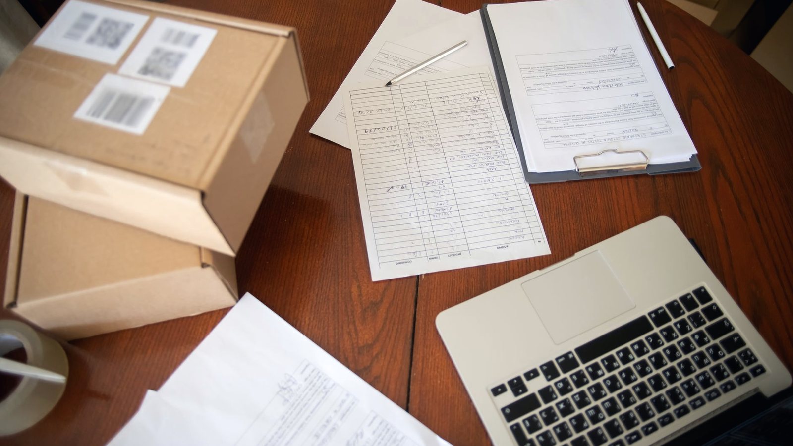 Desk with shipping paperwork, a laptop and labeled parcels