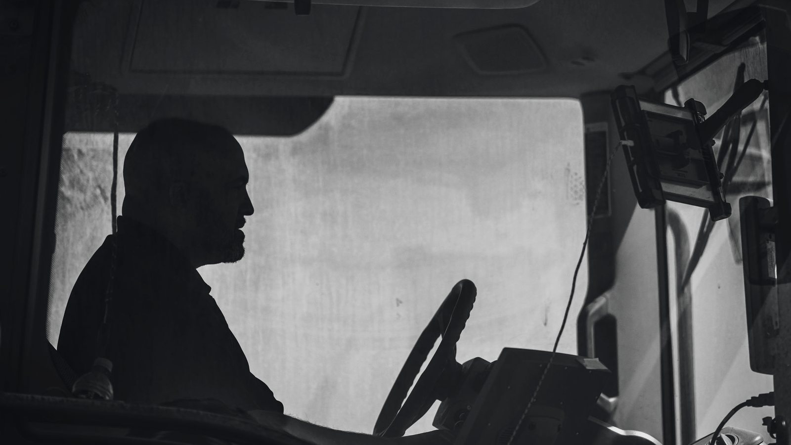 Black-and-white silhouette of a truck driver behind the wheel in the cab