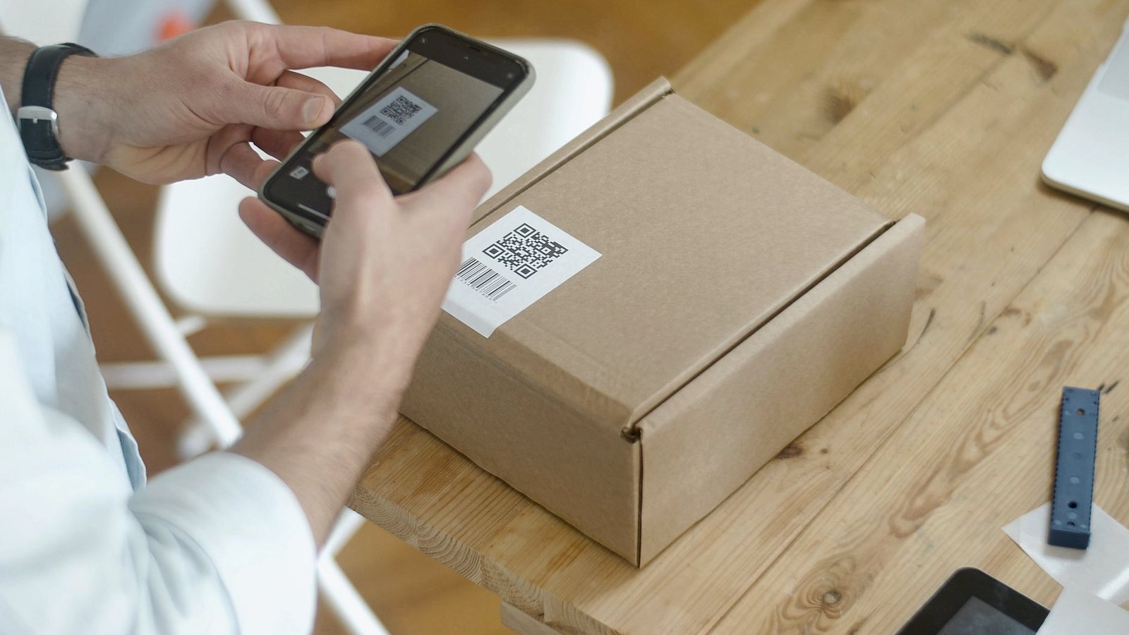 Hands scanning a barcode label on a cardboard box with a smartphone