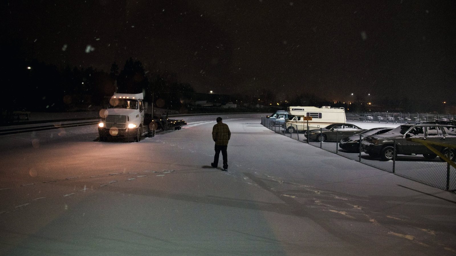 Lone person walking toward a parked truck in an empty, snowy lot at night
